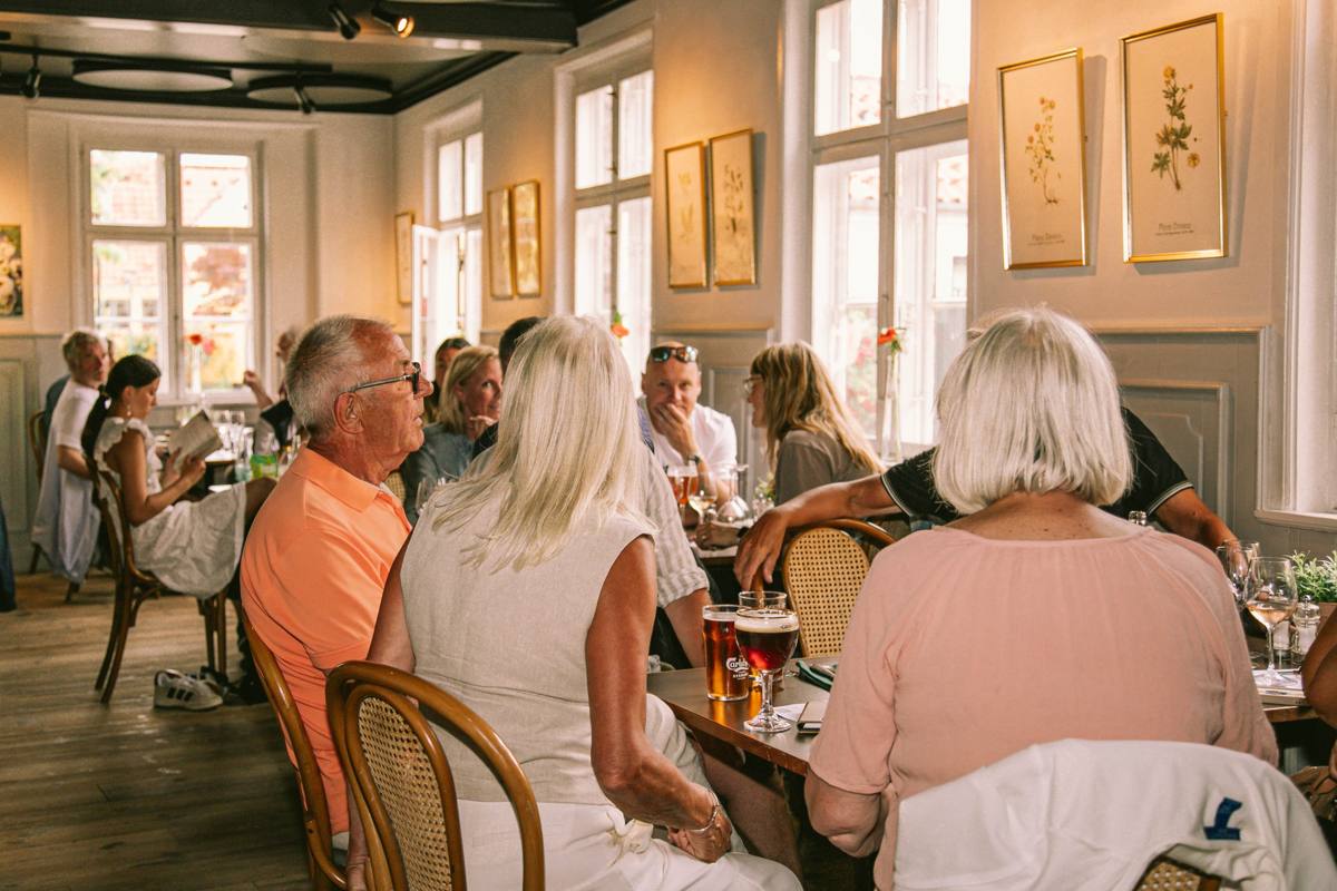 Gæster nyder frokost i den solbeskinnede spisestue på Beghuset under indrammede botaniske print