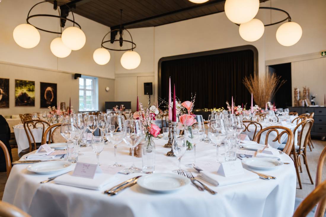 Runde borde med hvidt lærred, lys og lyserøde blomster i Beghusets Teatersal